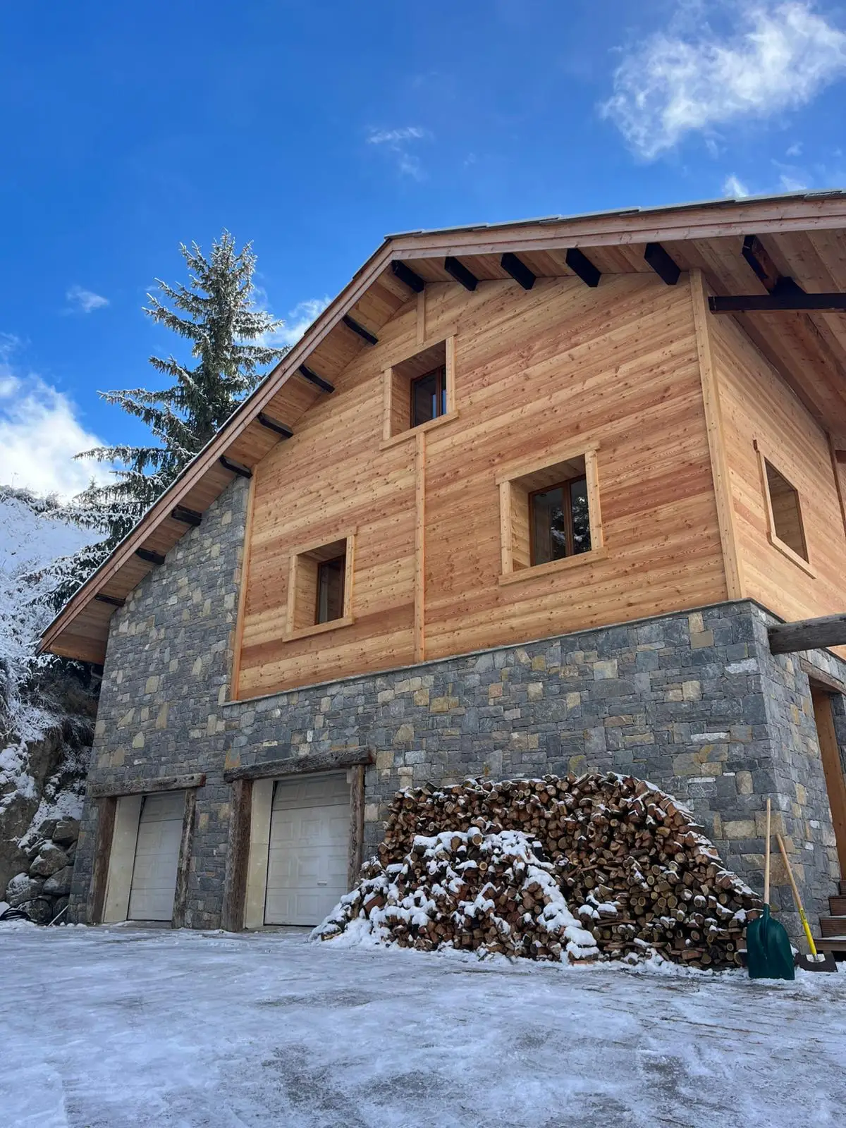 Façade en pierre et bois de mélèze du chalet Le Chantelevent à Vars sous un grand soleil, bordée par un parking enneigé.