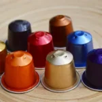 Capsules de café colorées type Nespresso disposées en cercle sur une table en bois