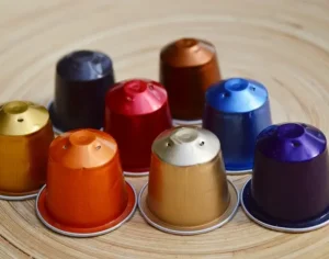 Capsules de café colorées type Nespresso disposées en cercle sur une table en bois