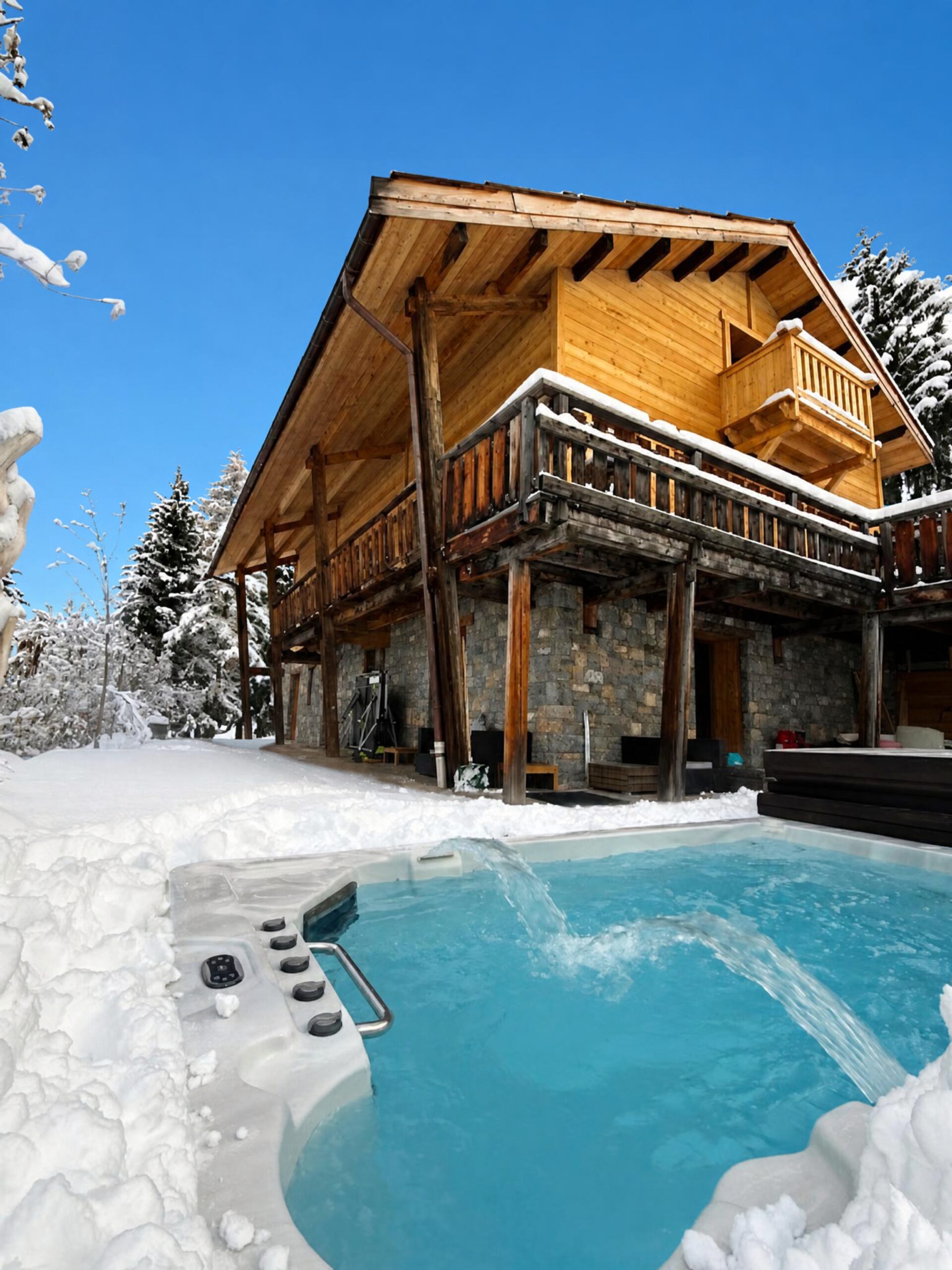 Façade sud du chalet Chantelevent à Vars sous la neige, avec au premier plan le spa de nage et des sapins enneigés